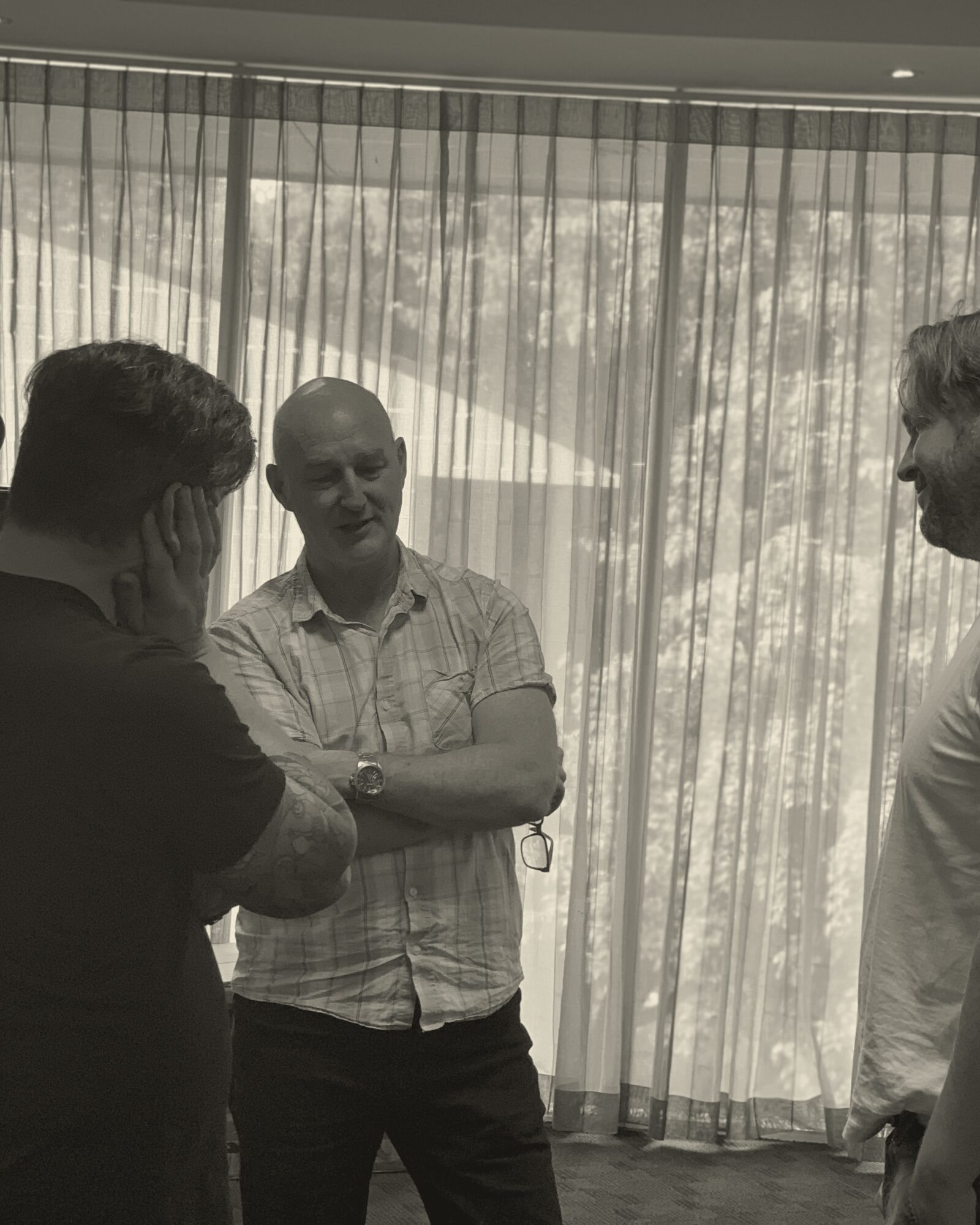 Three OST practitioners in conversation by a sunlit window during a break in a workshop.